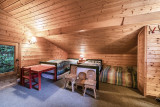 Chambre mansardée avec trois lits, table, petites chaises en bois, fenêtre